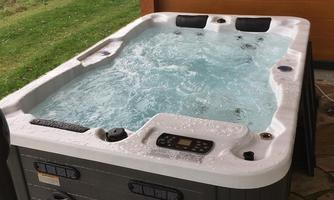 A hot tub with bubbling water stands on a terrace. In the background, green meadows and trees are visible.