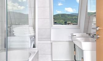 A modern bathroom with a bathtub and a shower. A large window view of the landscape provides daylight.