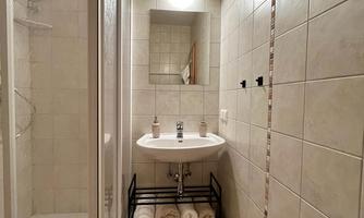 A modern bathroom with a shower and a sink. Towels are neatly placed on a shelf under the sink.