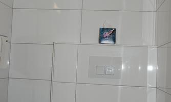 A modern bathroom with white tiles and a toilet. On the wall, there is a hairdryer and some sanitary fixtures.