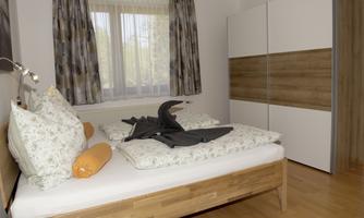 A cozy bedroom with a wooden bed, beautiful pillows, and a modern wardrobe. The window lets in plenty of daylight and gives the room an inviting atmosphere.