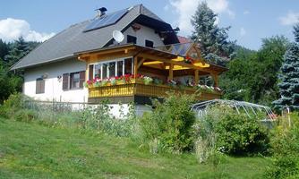 A house with a balcony adorned with flowers. In the background, trees and a blue sky can be seen.