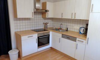 A modern kitchen with white cabinets and a wooden countertop. It is equipped with a stove, sink, and dishwasher.