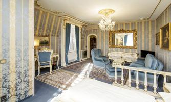 An elegant room with striped walls and a chandelier. There are cozy armchairs and a pretty window with curtains.