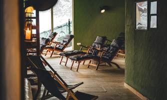 A relaxing room with wooden loungers and a cozy atmosphere. Soft lighting and large windows offer a view outside.