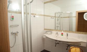 A modern bathroom with a shower and a rounded sink. The walls are decorated with white tiles and elegant accents.