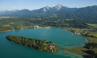 An impressive landscape with a clear lake and a wooded island. In the background, high mountains can be seen.