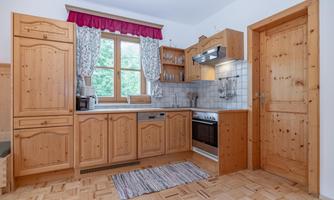 A cozy kitchen with wooden cabinets and a large window. The room is bright and cheerfully furnished.