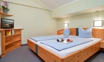 A modern bedroom with a double bed and cozy pillows. Next to the bed stands a shelf with a TV and books.