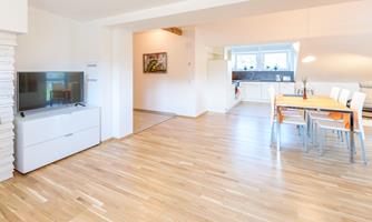 A bright and modern living environment with a hardwood floor. The room contains a television and a dining table with chairs.
