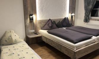A cozy bedroom with a double bed and an additional bed on the left side. The walls are made of wood, and there is soft lighting as well as curtains.