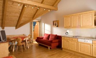 A cozy living room with a wooden ceiling and red furniture. The kitchen is modern and well equipped, ideal for a relaxing stay.