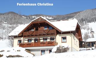 A cozy holiday home in a wintry landscape. The snow covers the roof and the surroundings are surrounded by mountains.