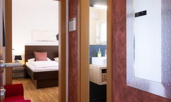A hotel room with a bed and a modern bathroom. The entrance area is bright and friendly designed.