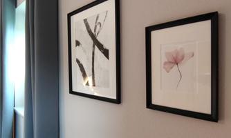 Two framed pictures hang on a bright wall. Next to a gray sofa are gray curtains.