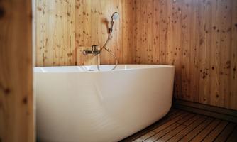 A modern bathroom with a freestanding bathtub. The walls are clad in wood, and the floor is made of wooden planks.