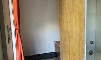 A bright entrance area with a wooden cabinet and a rug. Curtains in orange provide a colorful accent.