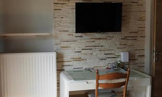A simple workspace with a table, a chair, and a television on the wall. The wall is decorated with a modern stone pattern.