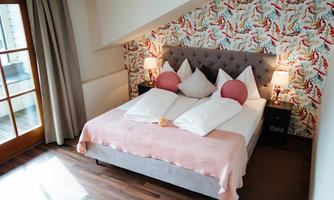 A cozy bedroom with a double bed and colorful cushions. The walls are decorated with a cheerful pattern, and there are two bedside lamps.