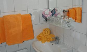 A small bathroom with white tiles and a sink. Orange towels and a hairdryer are clearly visible.