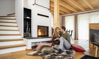 A cozy living room with a modern fireplace. A couple is sitting on the floor and enjoying a romantic time together.