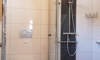 A modern bathroom with a shower and toilet. The walls are tiled in light colors, and the floor has an elegant pattern.