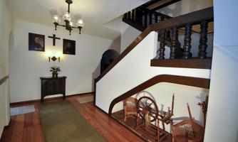 An inviting hallway with an elegant staircase and wooden details. Pictures hang on the walls and decorative furniture pieces are placed around.