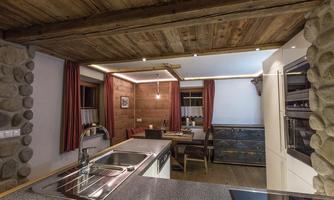 A cozy kitchen with wooden ceilings and stone walls. The room is inviting with a dining table and red curtains.