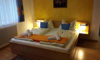 A cozy bedroom with a double bed and decorative pillows. The room has warm light and a calm atmosphere.