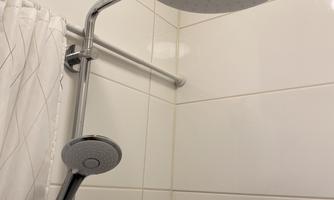 A modern shower with a large rain shower head and a handheld showerhead. The walls are clad with white tiles and the ceiling features wooden elements.