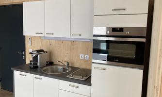 A modern kitchen with white cabinets and a stainless steel oven. The equipment includes a sink and a coffee machine.