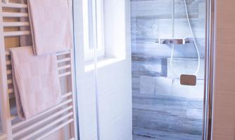 A modern shower with a glass partition and a rain shower head. Bright tiles and towels are visible in the background.