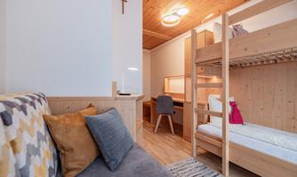 A modern room with a loft bed and a cozy sofa. The wooden walls and the simple decor create a relaxed atmosphere.