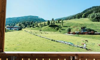 A picturesque landscape with green meadows and gentle hills. In the background, cows and a farmhouse can be seen.