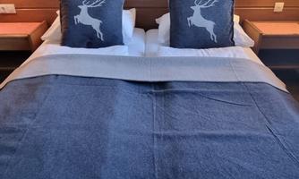 A cozy bed with two decorative pillows and a gray blanket. The pillows feature stylized deer motifs.