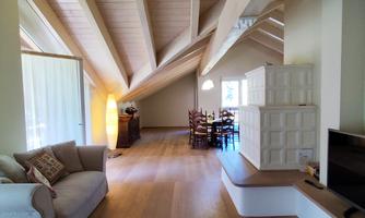 A bright living room with a modern, open layout. The space features wooden floors and high ceilings with exposed beams.