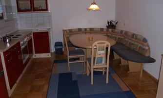 A cozy kitchen with a round table and a padded bench. The red kitchen cabinets and the wooden floor give the room a friendly atmosphere.