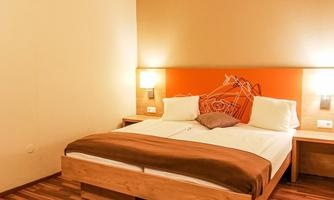 A modern bedroom with a large bed and wooden floor. The walls are painted in warm tones and there are nightlights on both sides of the bed.