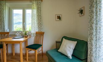 A cozy living space with a table, two chairs, and a green sofa. The window offers a beautiful view of the landscape.