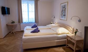 A bright and cozy bedroom with two single beds and a television. The windows provide natural light, and the decor is modern and inviting.