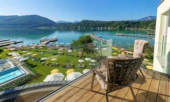 A beautiful view of a clear lake with docks and sunny loungers. In the foreground, there is a comfortable chair on a balcony.