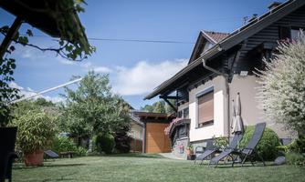A cozy garden with a house and sun umbrellas. The surroundings are green and inviting, perfect for relaxing.