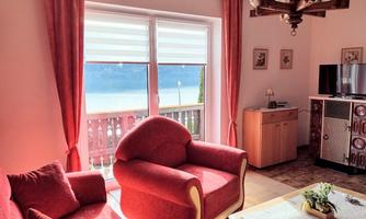 A cozy living room with red furniture and a view of the water. Large windows provide plenty of daylight.