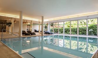 An elegant indoor pool with modern lighting and generous windows. Relaxed loungers invite you to linger.