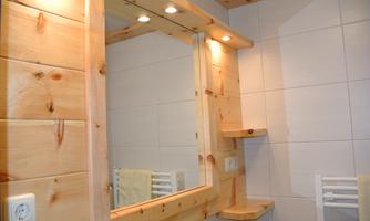 A modern bathroom with a wooden mirror and soft lighting. A bright atmosphere with white tiles and a chair.