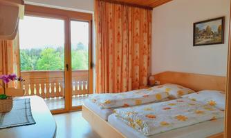 A cozy bedroom with two beds and a balcony. Large windows let in plenty of light and offer a view of the green surroundings.