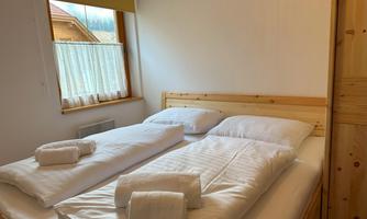 A cozy bedroom with two single beds and a towel. Light streams through the window, creating a bright atmosphere.