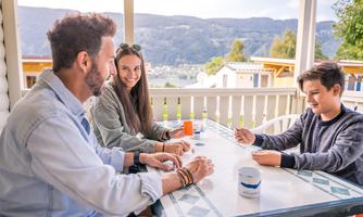 A group of three people is sitting at a table and playing cards. In the background, there is a beautiful view of the mountains.