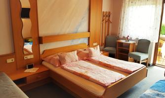 A cozy bedroom with a large bed and wooden-colored furniture. The room has windows that let in natural light.
