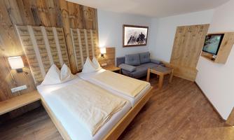 A modern hotel room with two beds and a cozy living area. Wooden walls give the space a warm atmosphere.